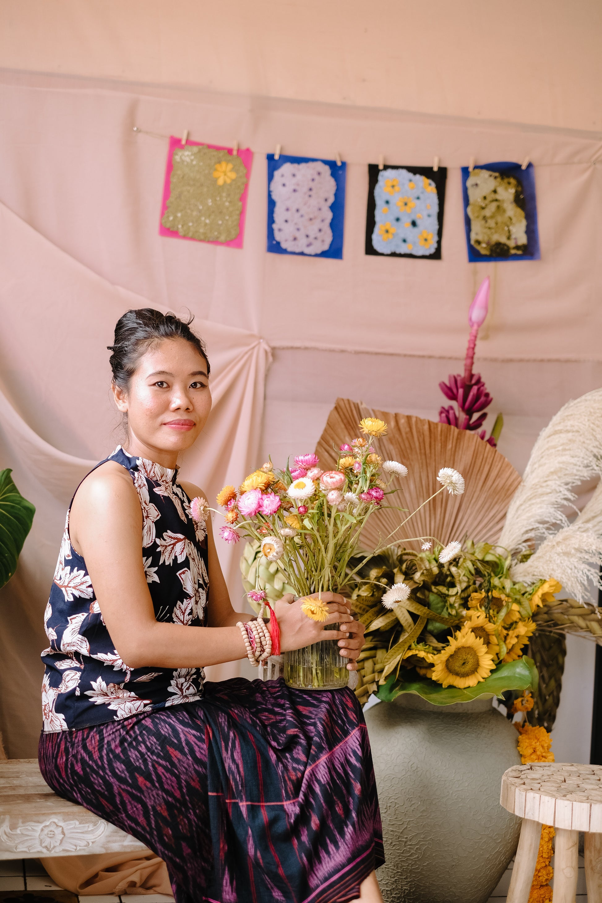 Artist Novi sitting in her studio with environmentally friendly recycled paper decorations visible in the background.