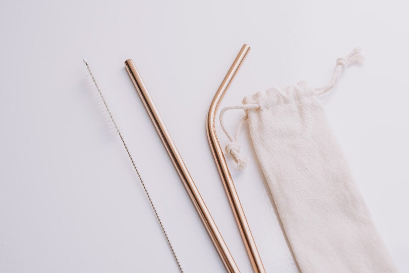 Two environmentally friendly gold straws on the counter with a whispy cleaner and a sleek carrying bag.
