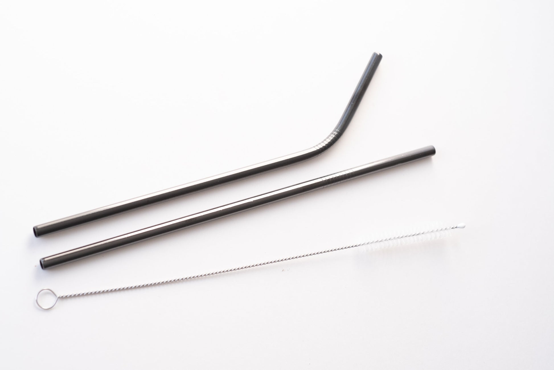 Two sustainable silver straws on a counter with a wispy cleaner.