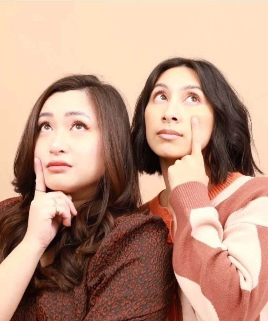Angela Non and Ariana Kempis, the Asian American co-hosts of the brb crying podcast, posing with their fingers on their faces as if crying.