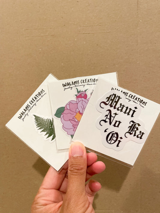 The sticker options are one that says "Maui No Ka 'Oi" in a calligraphic font, a blooming pink flower and a fern.