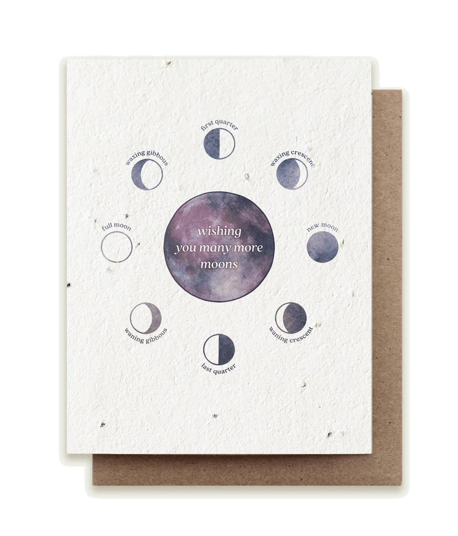 A beautifully painted eco-friendly seed card reads "wishing you many more moons" on a cosmic circle in the center. It's surrounded by small moons in different phases.