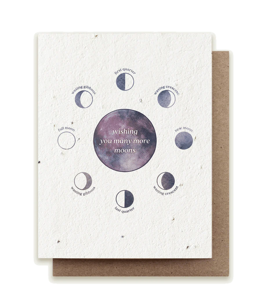 A beautifully painted eco-friendly seed card reads "wishing you many more moons" on a cosmic circle in the center. It's surrounded by small moons in different phases.