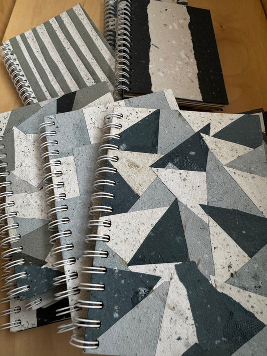 Stack of eco-friendly spiral notebooks with blank pages. Covers have decorative patterns of recycled paper.